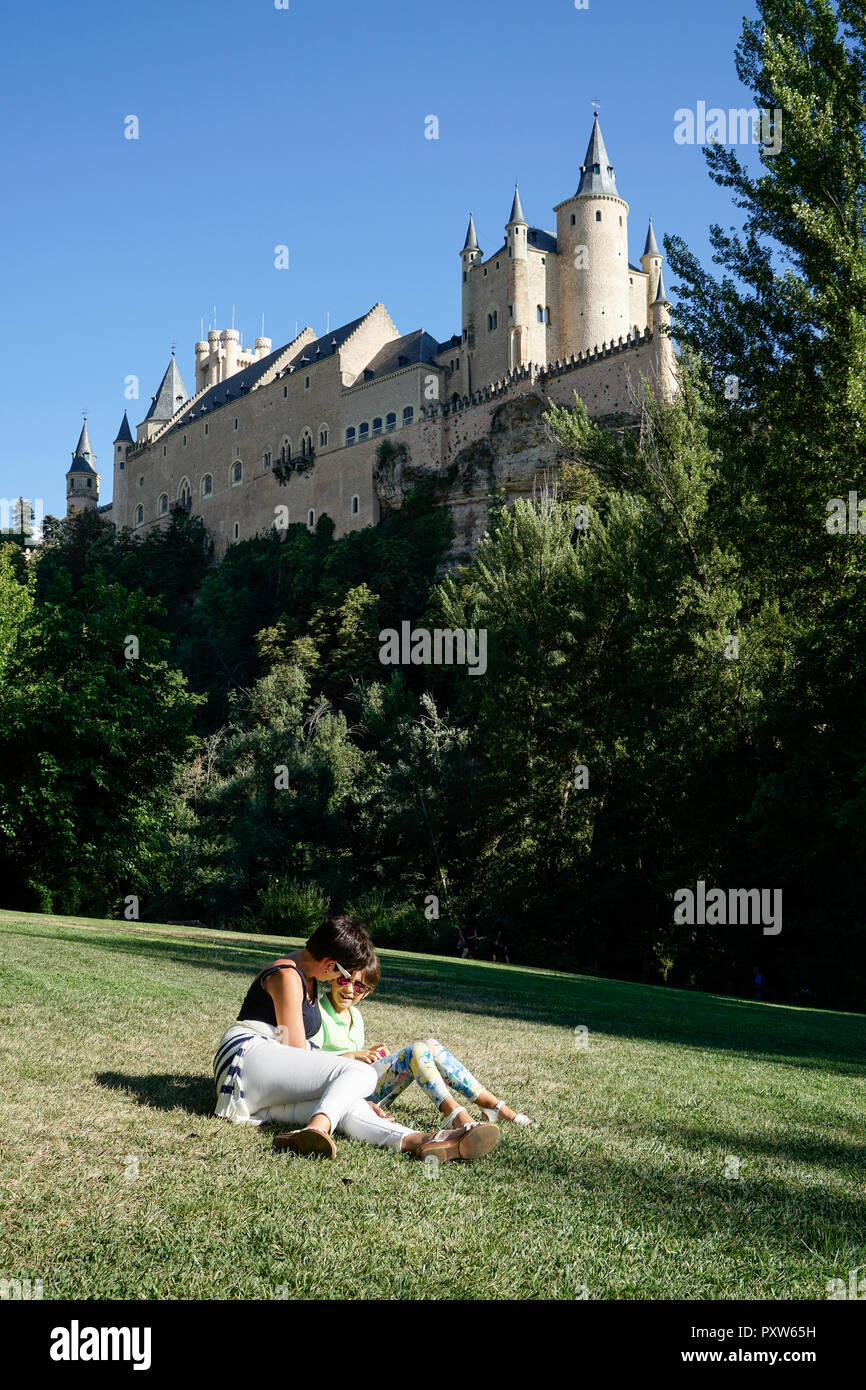 Spanien, Kastilien und Leon, Segovia, Mutter und Tochter auf Gras in der Nähe von Alcazar von Segovia sitzen Stockfoto