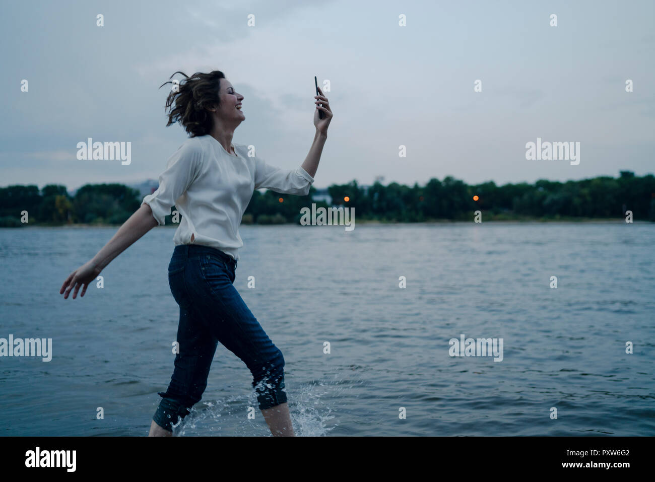 Lachende Frau am Flußufer läuft, Sie ihr Smartphone Stockfoto
