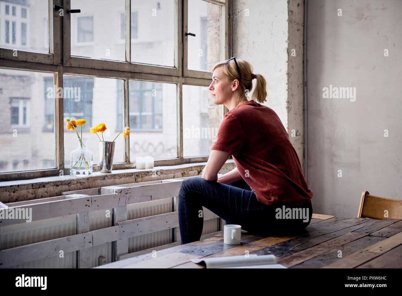 Frau sitzt am Schreibtisch im Loft auf der Suche durch das Fenster Stockfoto