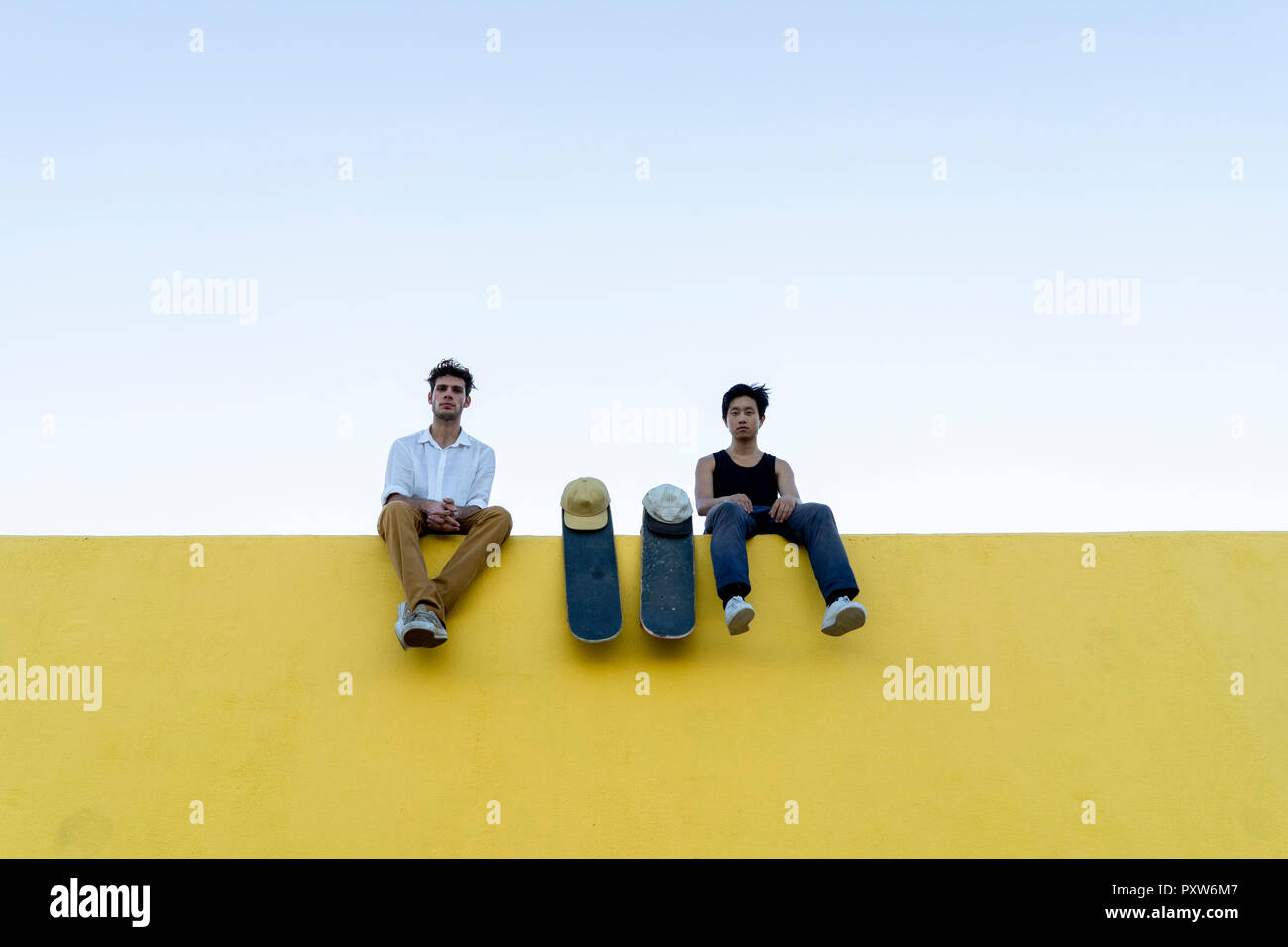 Zwei junge Männer mit skateboards sitzt auf einem hohen gelbe Wand Stockfoto