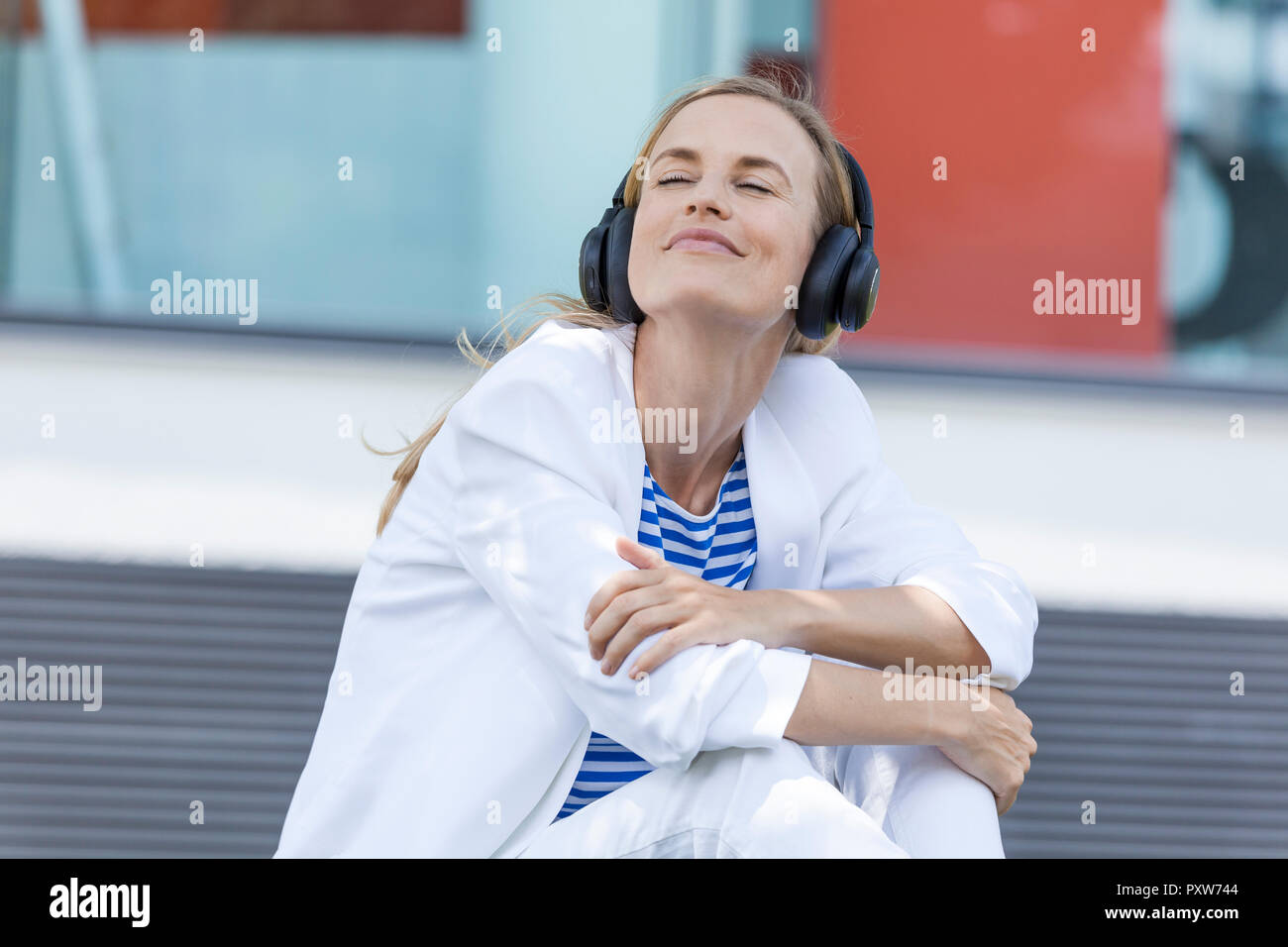 Lächelnde blonde Geschäftsfrau mit geschlossenen Augen, Liste Musik, Ohrhörer Stockfoto