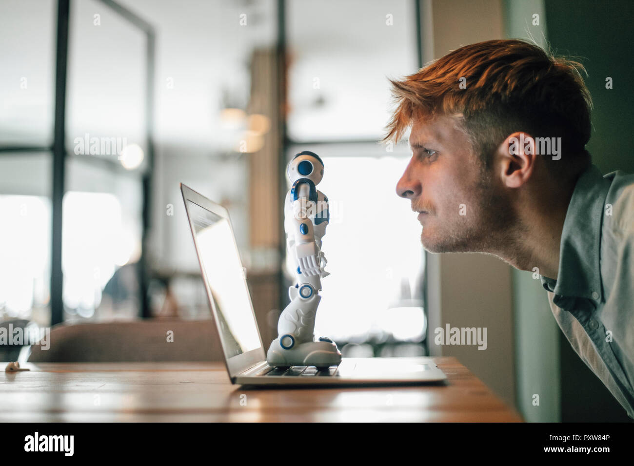 Mann an Spielzeug Roboter suchen, stehend auf seinem Laptop Stockfoto