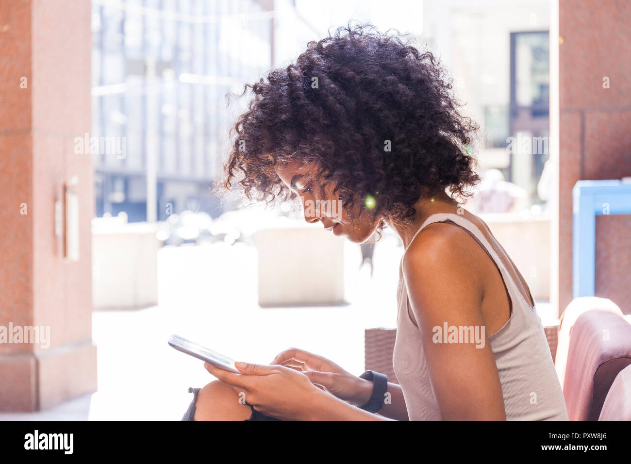 Junge Frau mit lockigem Haar im Straßencafe mit digitalen Tablet sitzen Stockfoto