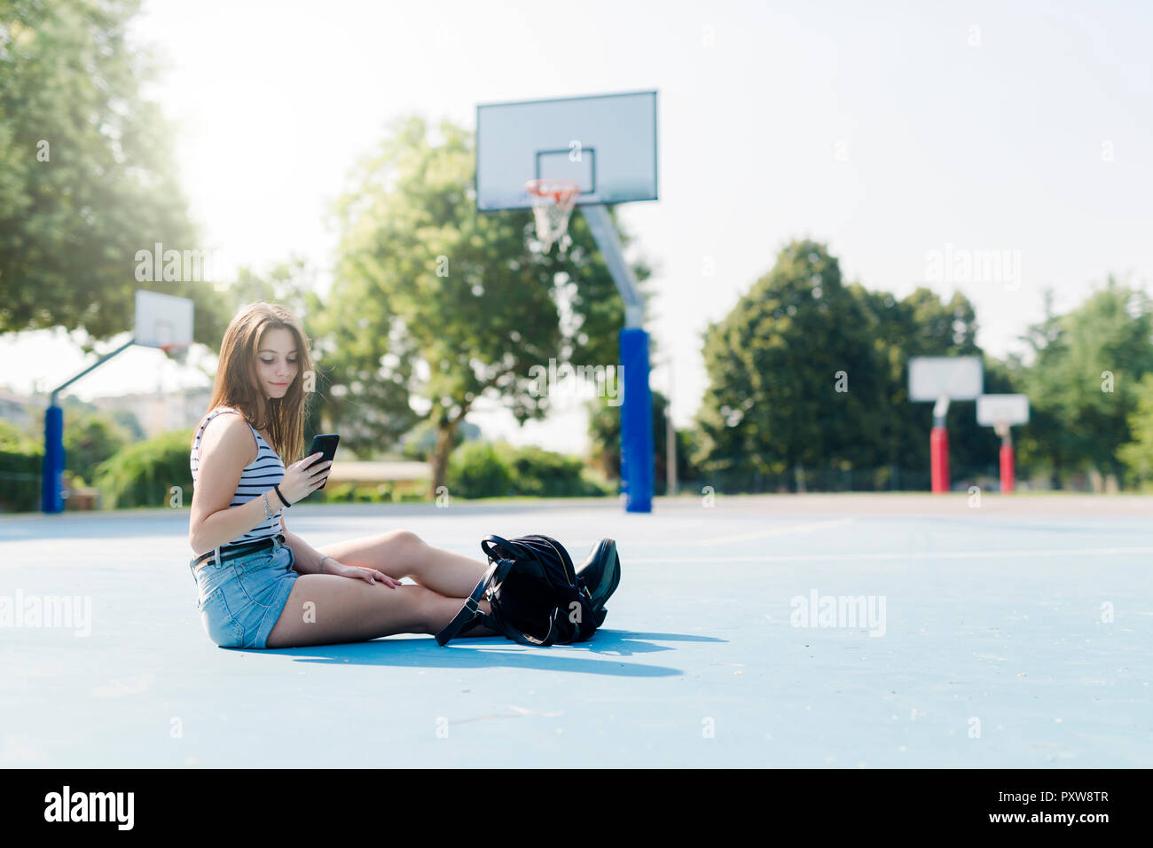 Junge Frau mit Rucksack auf Sportplatz mit Handy Stockfoto