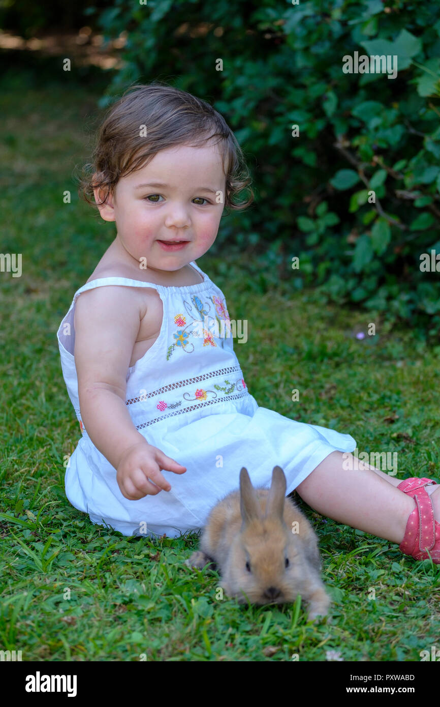 Portrait von Inhalt baby girl sittting auf einer Wiese mit jungen Bunny Stockfoto
