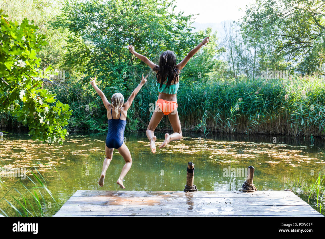 Zwei unbeschwerte Mädchen springen in Teich Stockfoto