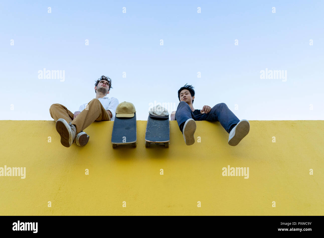 Zwei junge Männer mit skateboards sitzt auf einem hohen gelbe Wand Stockfoto