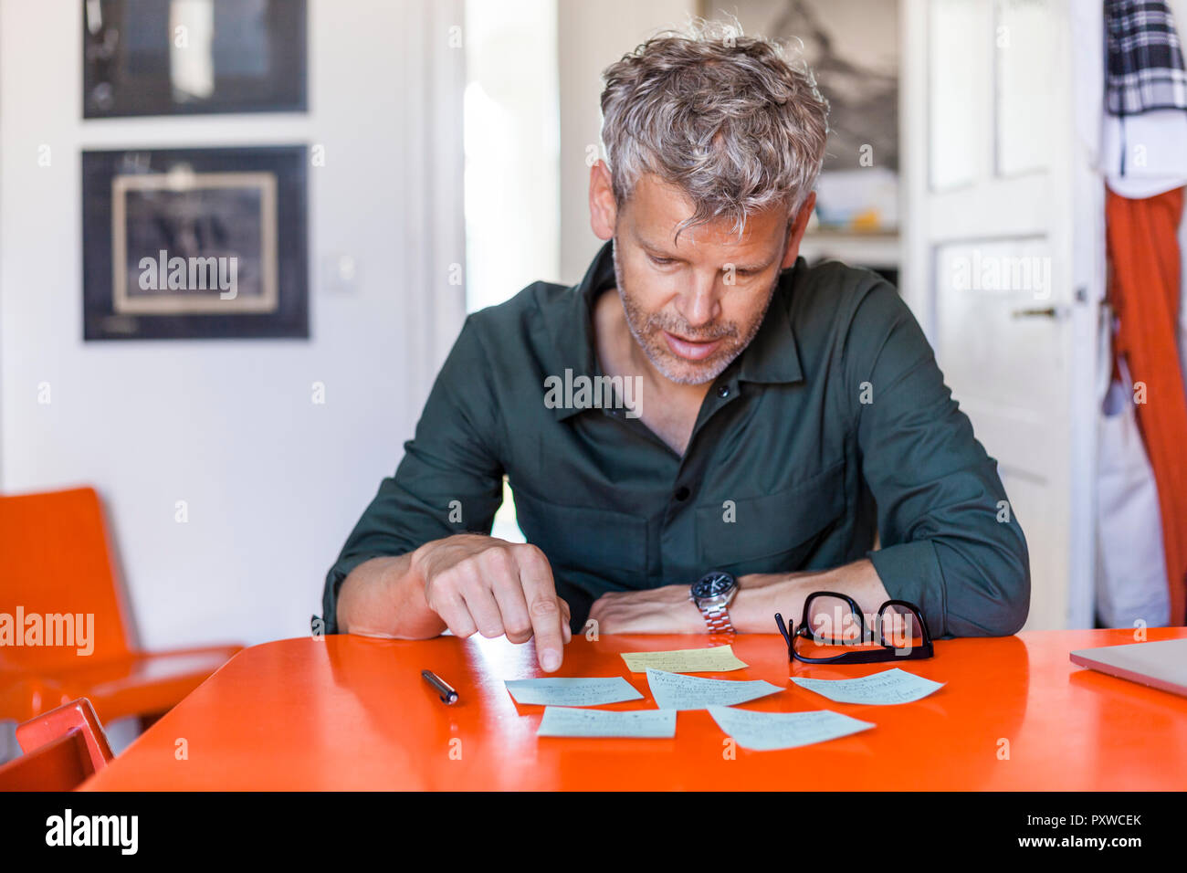 Reifer mann am Tisch zu hause sitzen auf der Suche nach Notizblöcke. Stockfoto