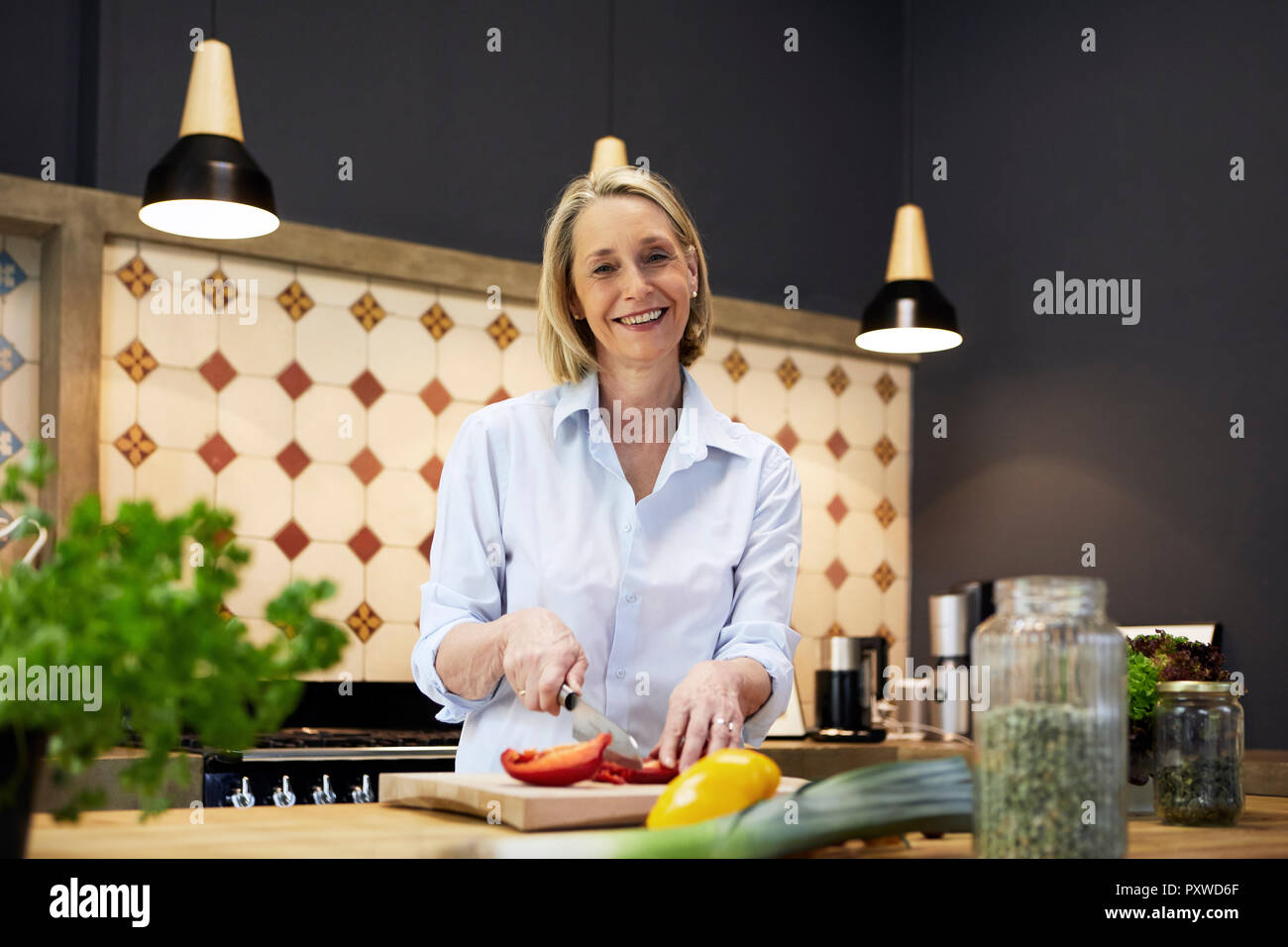 Portrait von lächelnden reife Frau hacken, Paprika in der Küche Stockfoto