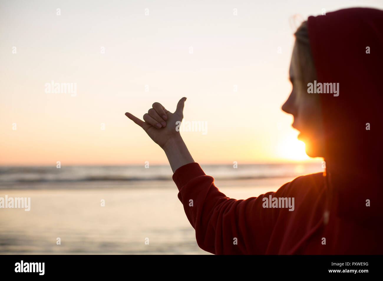 Junge Frau das Tragen der roten Kapuzenjacke am Strand bei Sonnenuntergang, lose Geste hängen Stockfoto
