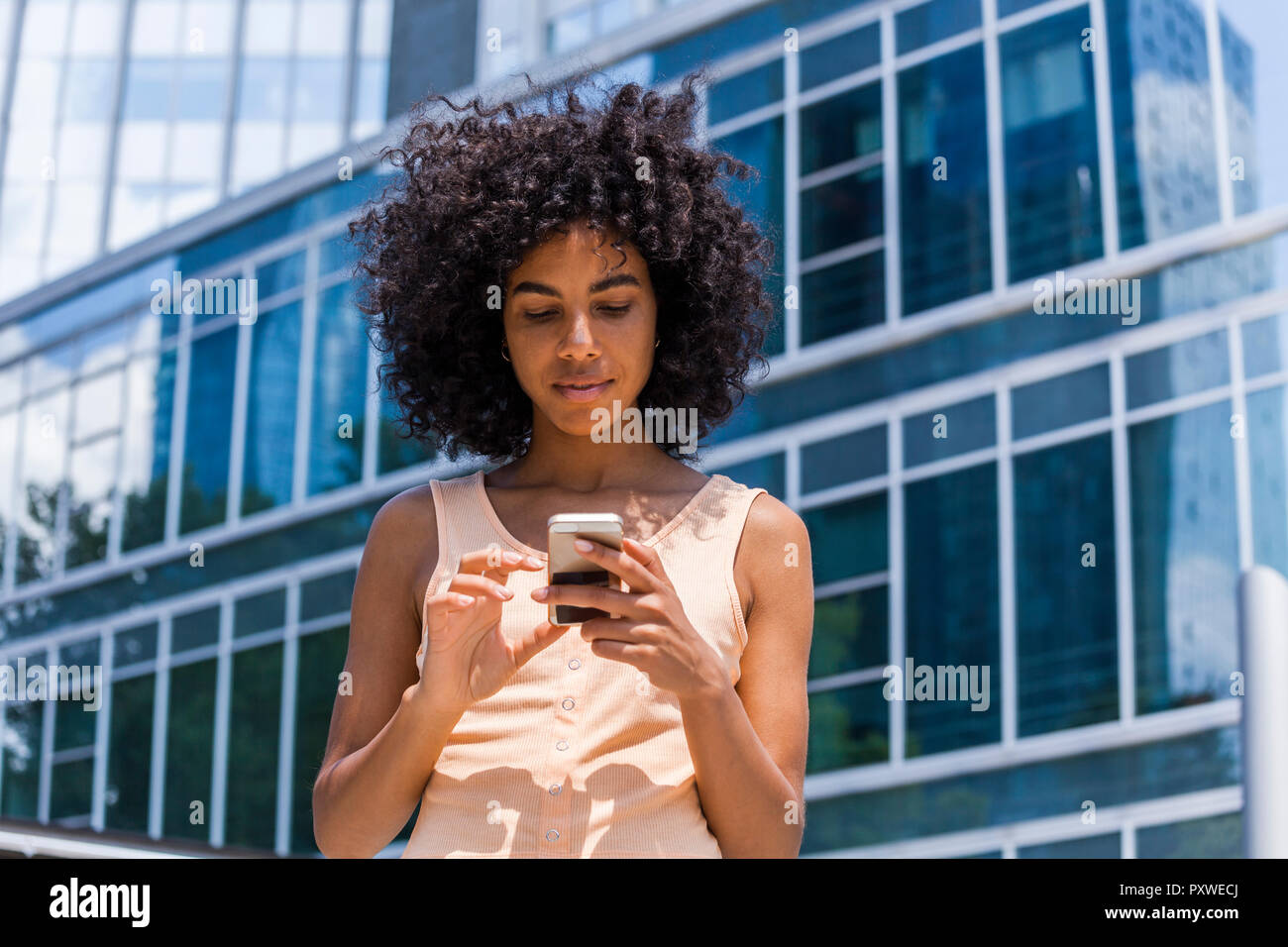Deutschland, Frankfurt, Porträt der jungen Frau mit dem lockigen Haar mit Smartphone Stockfoto