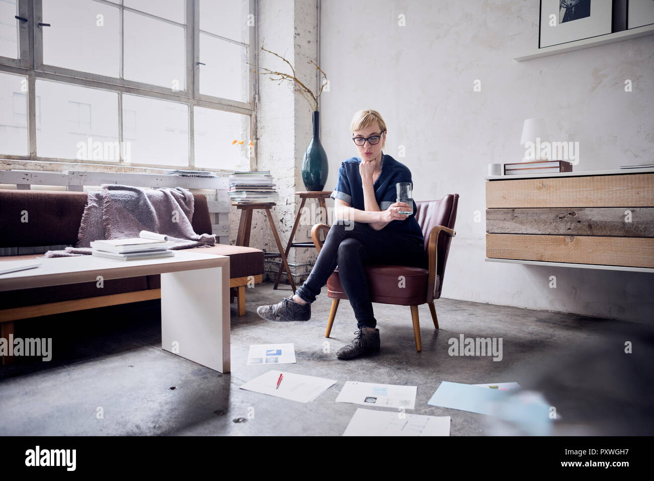 Frau sitzt auf einem Sessel im Loft auf Papier auf dem Boden suchen Stockfoto