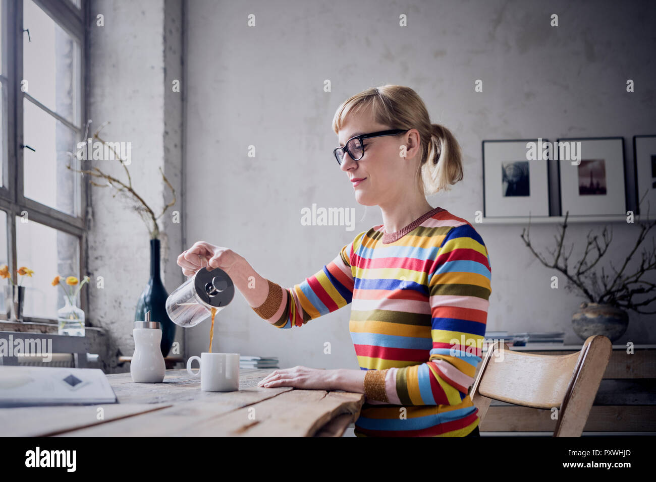 Frau gießen Kaffee in eine Tasse am Schreibtisch in einem Loft Stockfoto