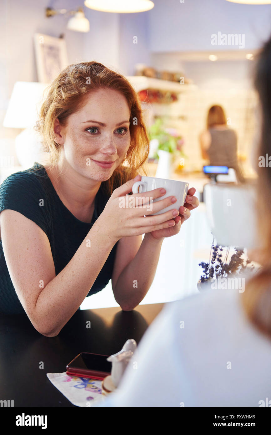 Lächelnde junge Frau trinkt Kaffee mit Freunden im Cafe Stockfoto
