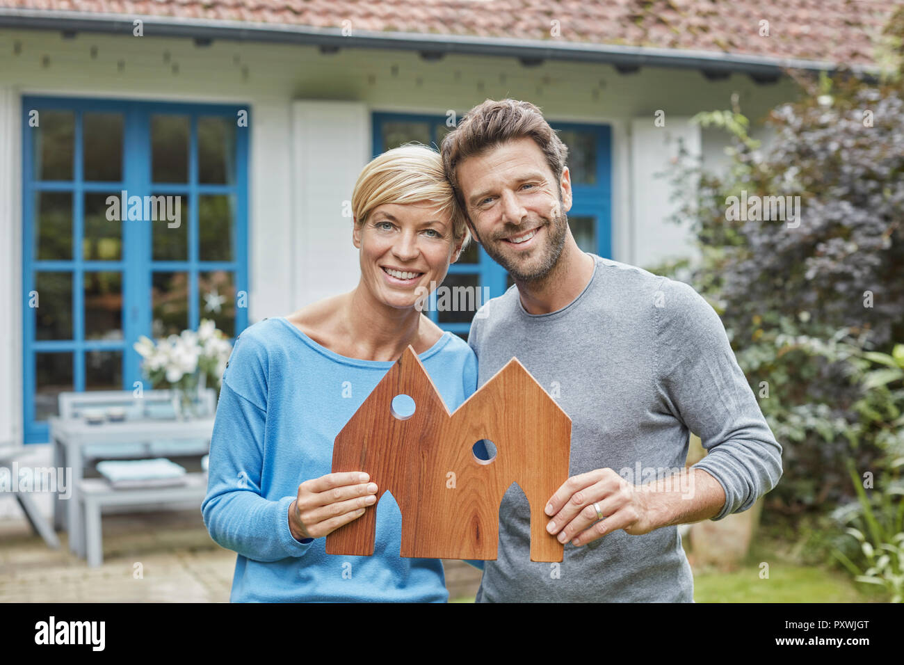 Portrait von lächelnden Paar steht vor ihrem Haus holding Haus Modell Stockfoto