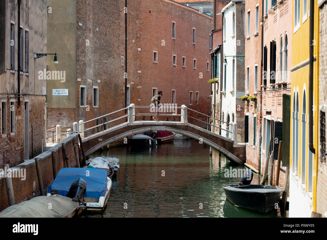 Eine einzelne touristische Überqueren der Steinbrücke über einen Kanal in einem ruhigen Teil von Venedig im Sommer. Stockfoto