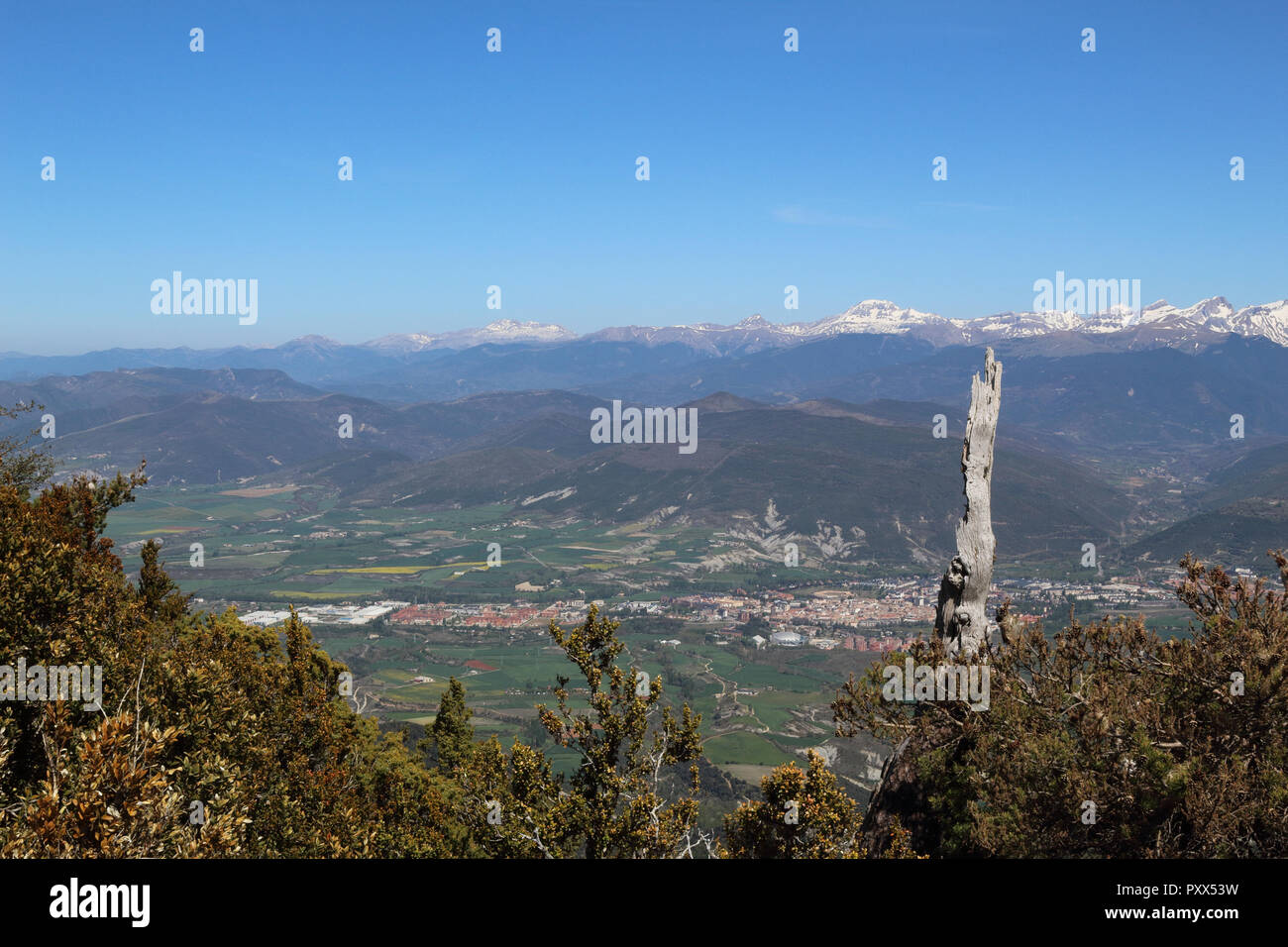 Eine Landschaft mit schneebedeckten Pyrenäen und ein weites Tal mit blauen bewölkten Himmel und einige Büsche in den Peña Oroel, Region Aragon, Spanien Stockfoto