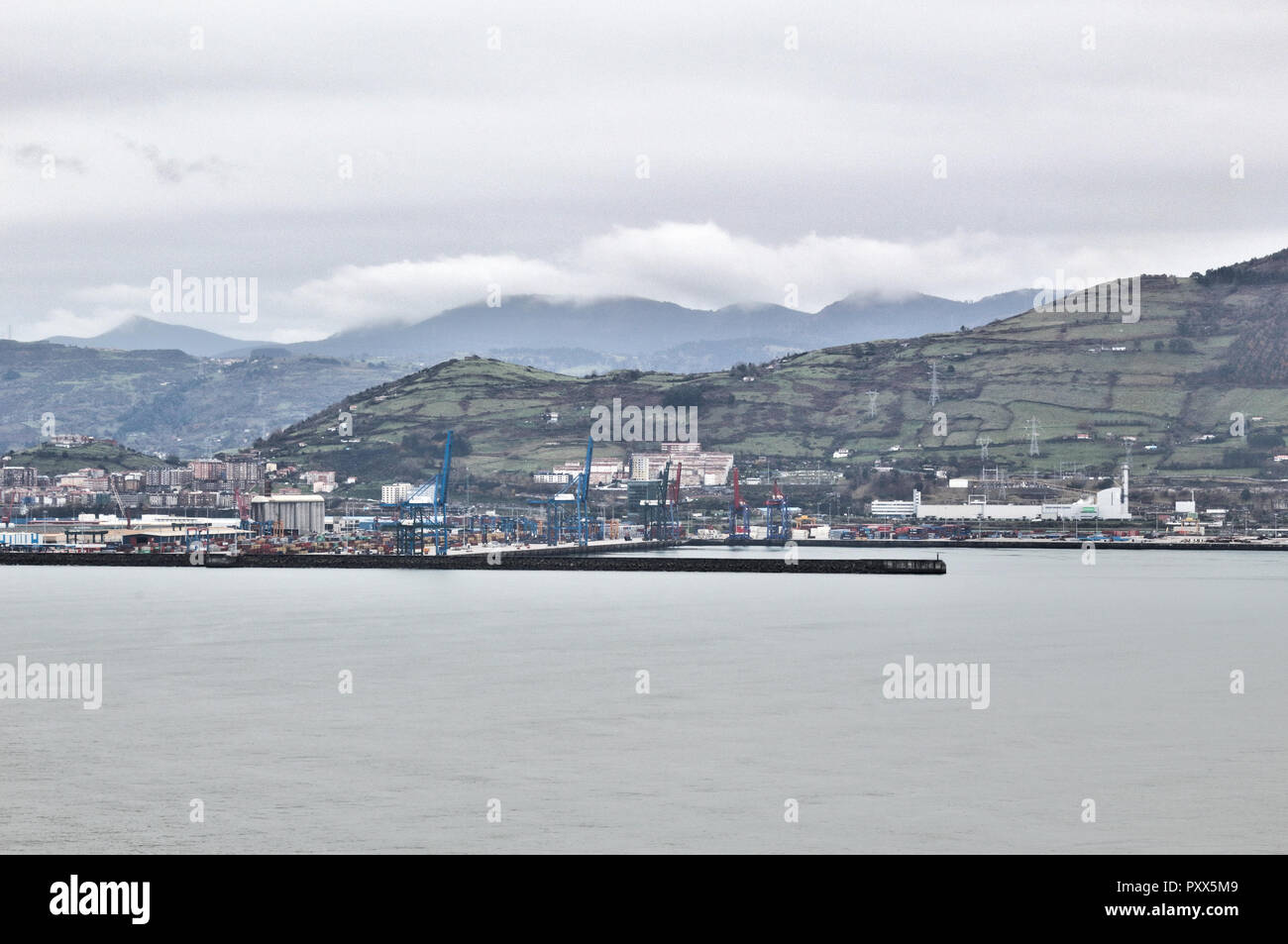 Zierbena Port mit grünen Hügeln im Hintergrund, Schuß vom Paseo de La Galea Promenade in Getxo, Baskenland, Spanien, während einer nebligen trüben Wintertag Stockfoto