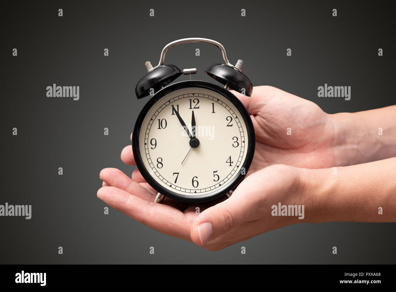 Hand hält die alte analoge Uhr, die fünf Minuten vor zwölf Uhr zeigt an, Stockfoto