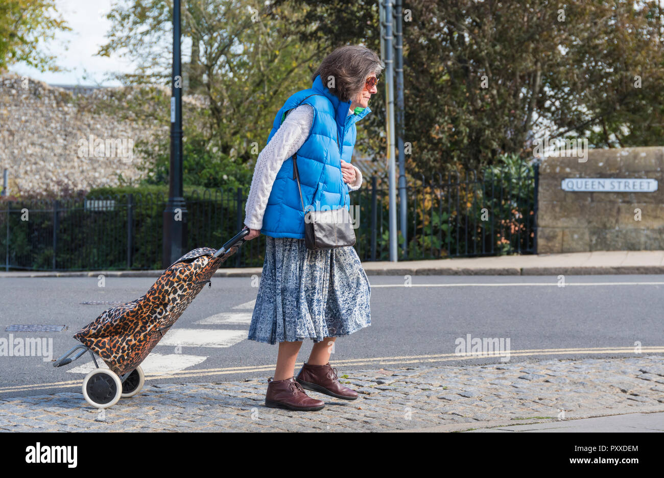Ältere Frau zu Fuß, während Sie einen Einkaufswagen in Großbritannien, Seitenansicht. Stockfoto