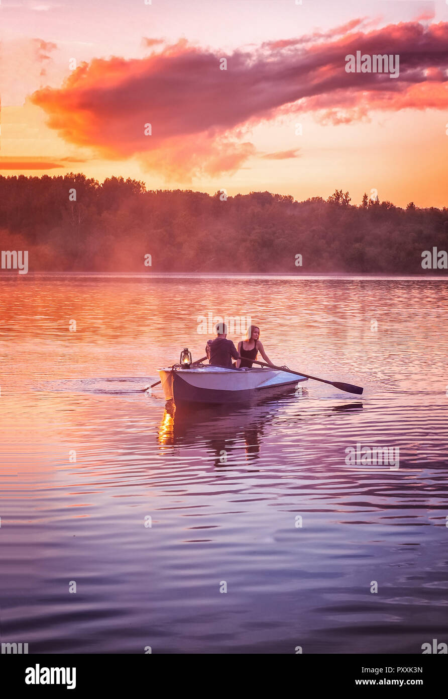 Paar in Love Ride in einem Boot auf dem See bei Sonnenuntergang. Romantischer Sonnenuntergang in der Goldenen Stunde. River Lake Nebel Liebespaar Ruderboot Datum beautifu Stockfoto