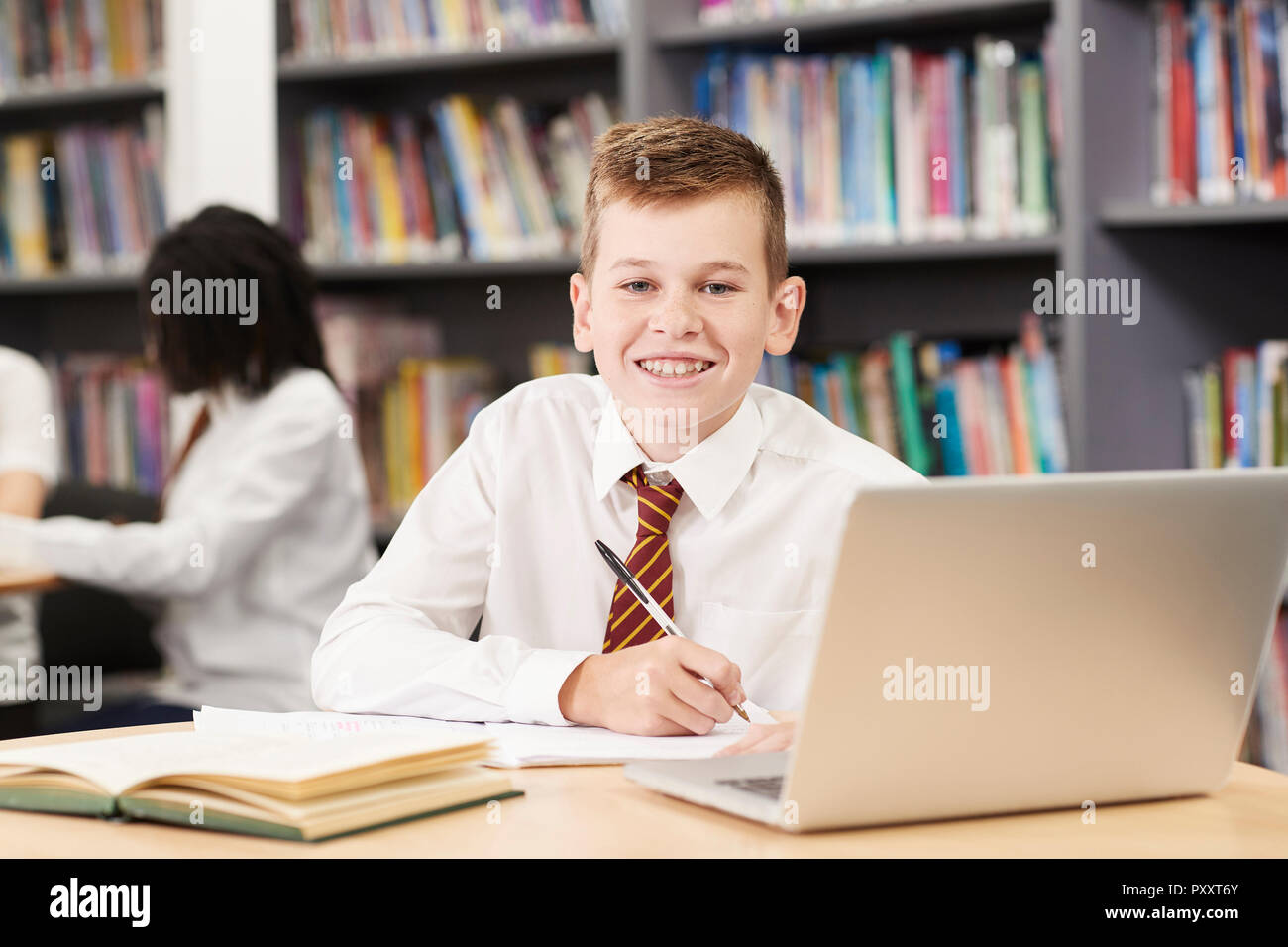 Portrait der männlichen High School Student trägt Uniform Arbeiten am Laptop in der Bibliothek Stockfoto