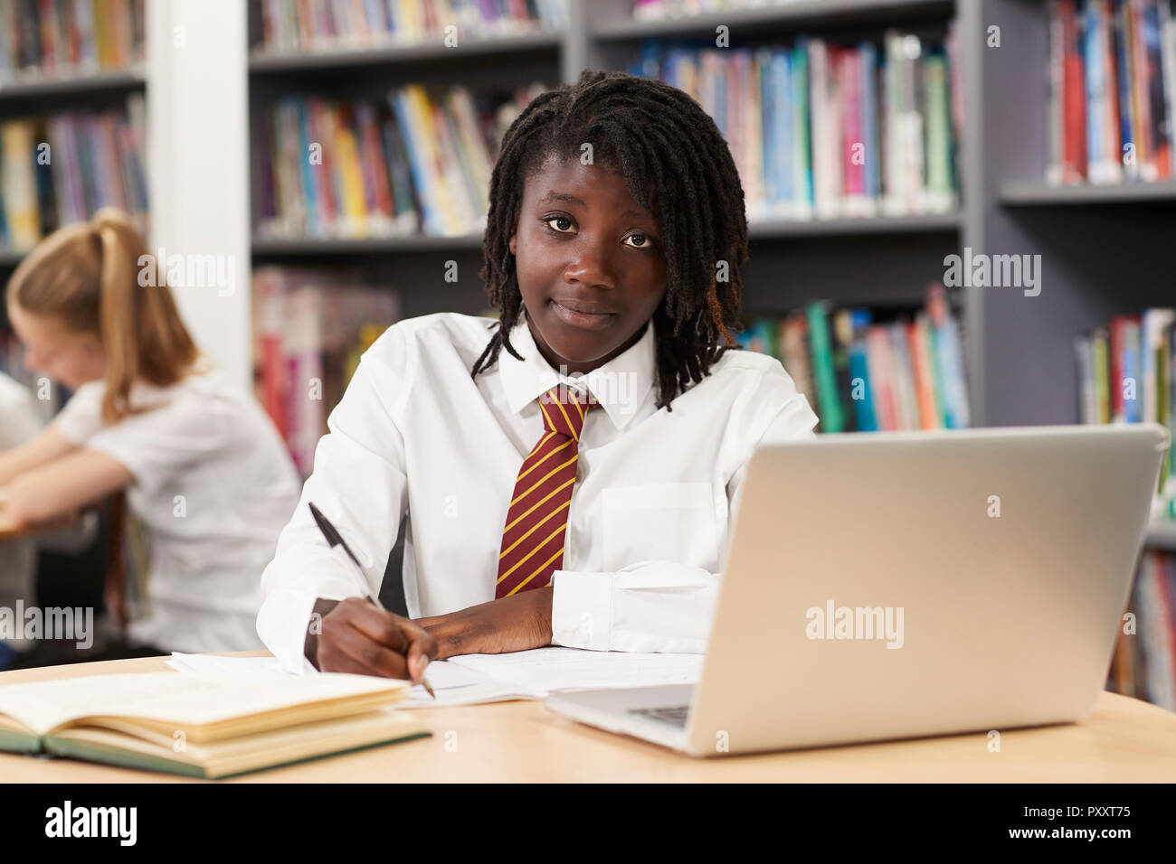 Portrait von weiblichen High School Student trägt Uniform Arbeiten am Laptop in der Bibliothek Stockfoto