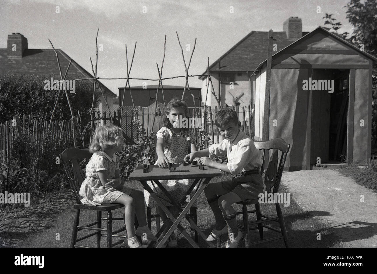 1950, historische, drei junge Kinder zusammen draußen im Garten sitzen spielen Domino an einem Tisch, England, UK. Stockfoto