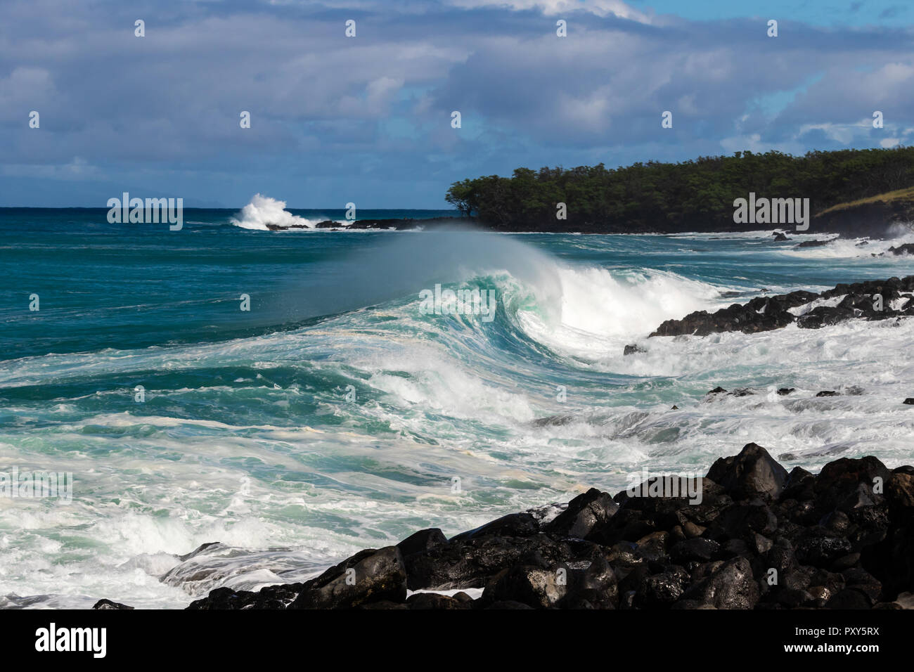 Eisstockschießen wave trailing Gischt brechen in der Nähe der Ufer auf Hawaii. Streifen im Hintergrund mit Felsen und Bäume. Bewölkter Himmel. Stockfoto
