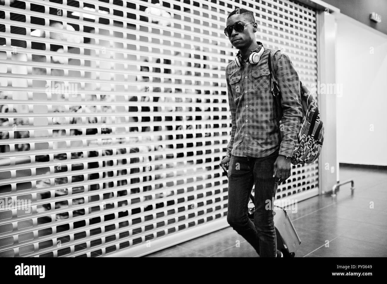 Afrikanische amerikanische Mann in kariertem Hemd, Sonnenbrillen und Jeans mit Koffer und Rucksack. Schwarzer Mann Reisender auf zollfrei. Stockfoto