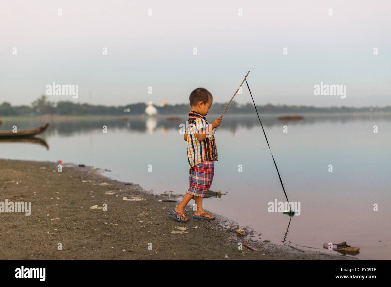 Kleiner Junge stehend auf Lakeshore spielen mit hausgemachten Angelrute, Mandalay, Mandalay, Myanmar Stockfoto