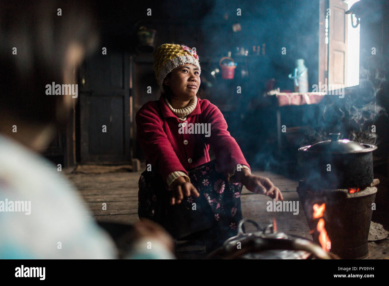 Junge Frau Hockend vor indoor Lagerfeuer und wärmende Hände, Myanmar, Shan, Myanmar Stockfoto