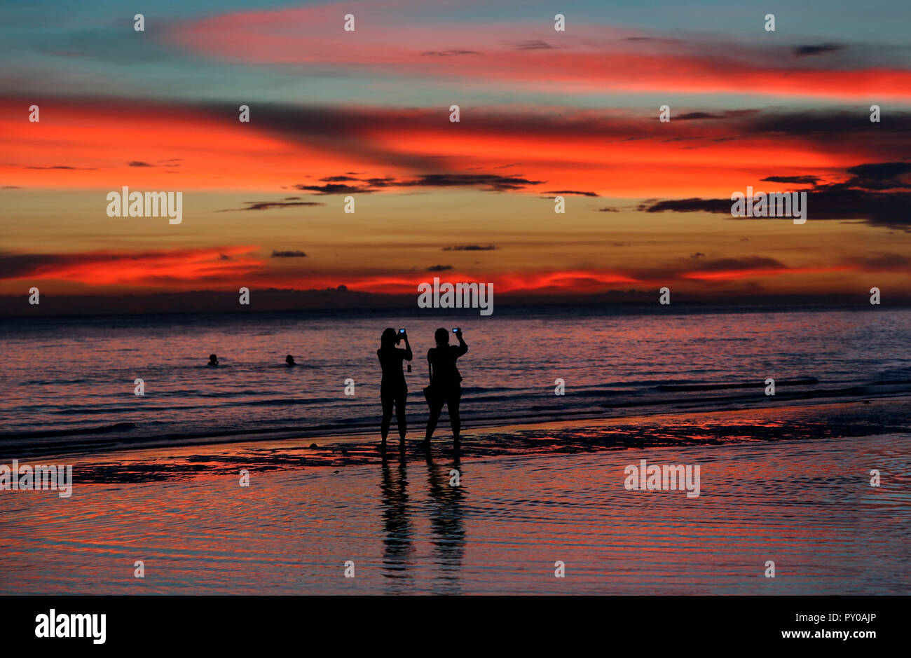 Silhouetten von zwei weiblichen Touristen fotografieren Sonnenuntergang am Strand, Boracay, Aklan, Philippinen Stockfoto