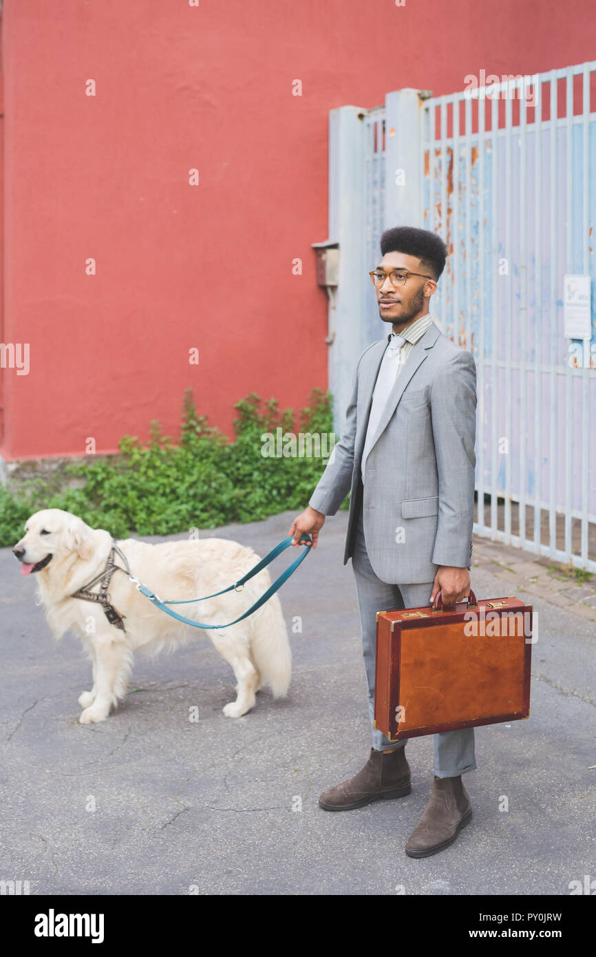 Junge schwarze Business man walking Outdoor mit Hund an der Leine zu arbeiten - Wirtschaft, Arbeit, Job Konzept Stockfoto