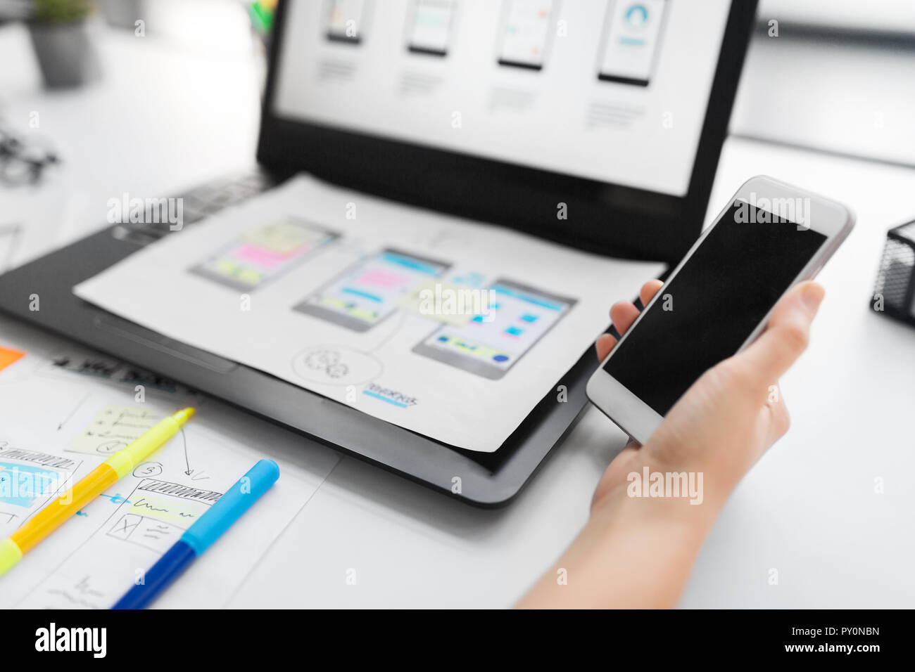 Web Designer mit Smartphone und Laptop im Büro Stockfoto