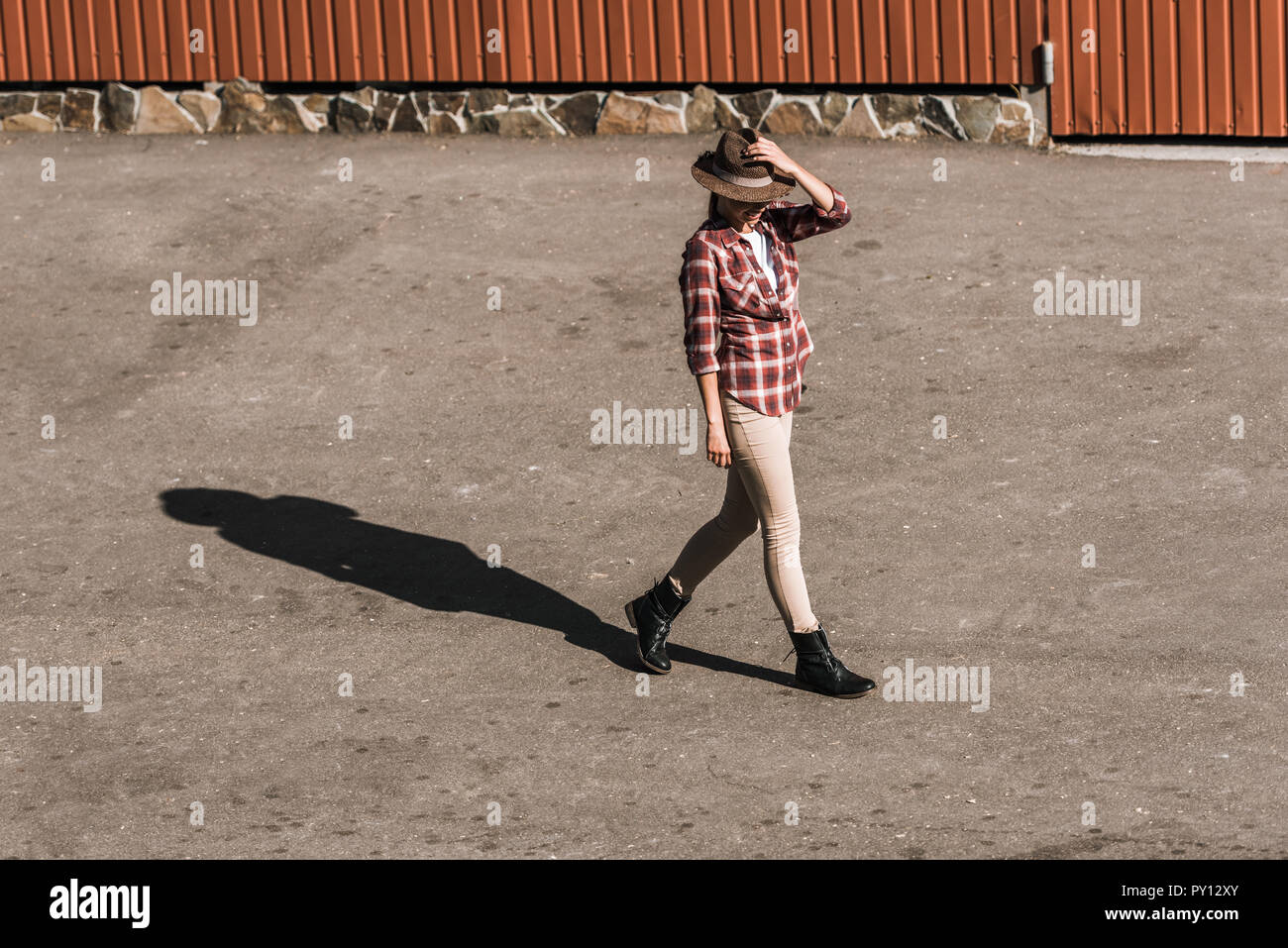 Attraktive Frau in kariertem Hemd berührt hat und zu Fuß in der Nähe der braunen Gebäude an der Ranch Stockfoto