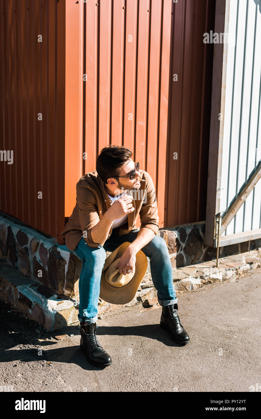 Stattliche Cowboy in Sonnenbrille sitzen und Rauchen Zigarette an der Ranch Stockfoto