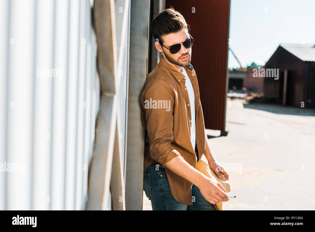 Stattliche Cowboy in der Sonnenbrille, die Zigarette und lehnte sich an die Wand an der Ranch Stockfoto