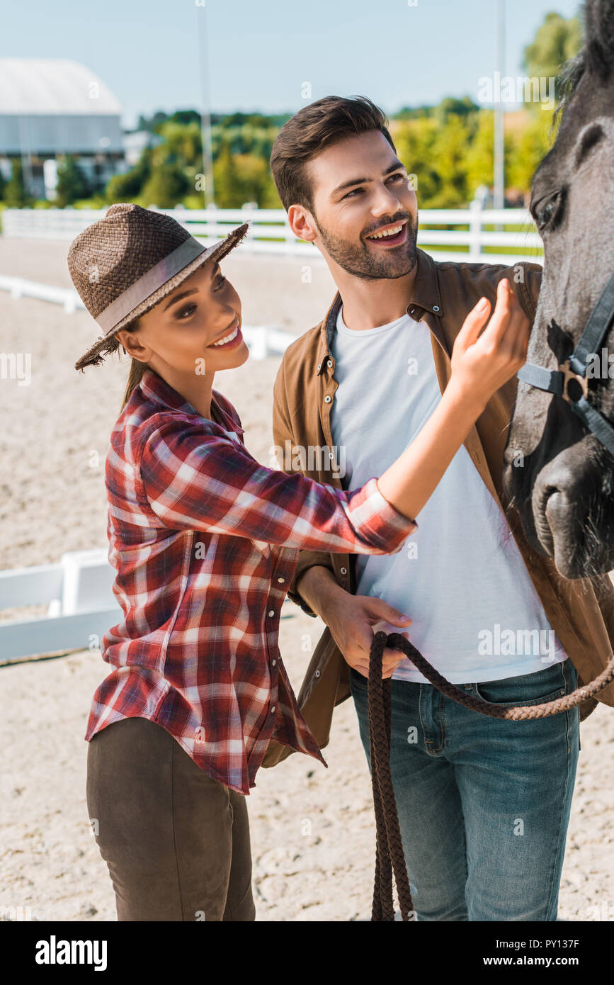 Lächelnd Cowboy und Cowgirl palming schwarzes Pferd an der Ranch Stockfoto