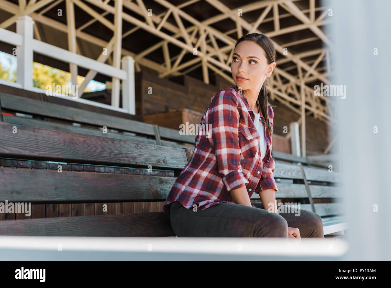 Schöne cowgirl in kariertem Hemd sitzt auf der Bank an der Ranch Stadion und Wegsehen Stockfoto