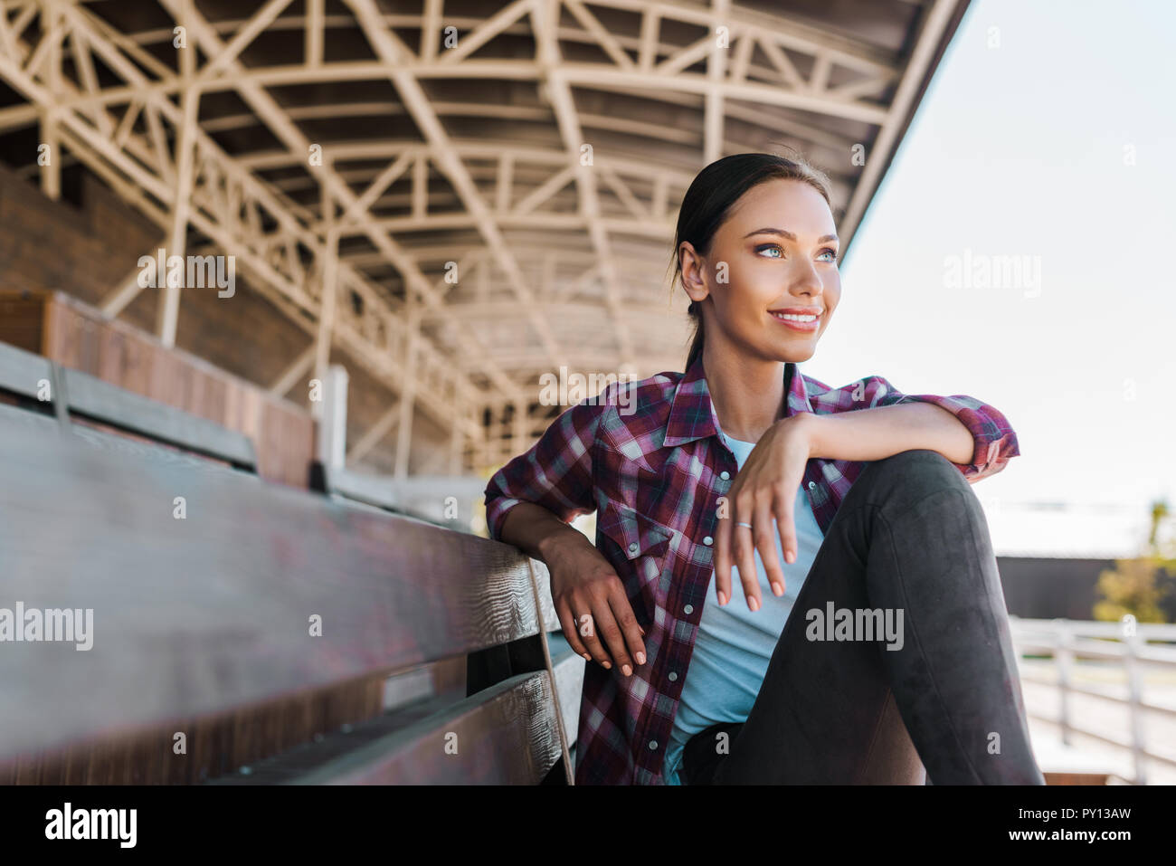 Attraktive Frau in kariertem Hemd sitzt auf der Bank an der Ranch Stadion und Wegsehen Stockfoto