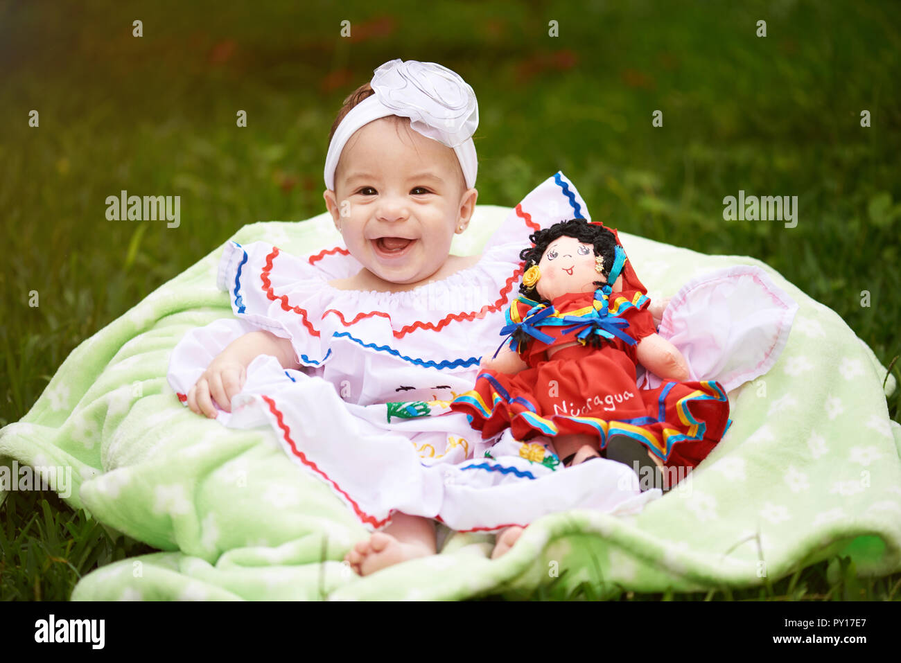 Glücklich lächelnde Mädchen mit Puppe sitzen auf grünem Gras Hintergrund Stockfoto
