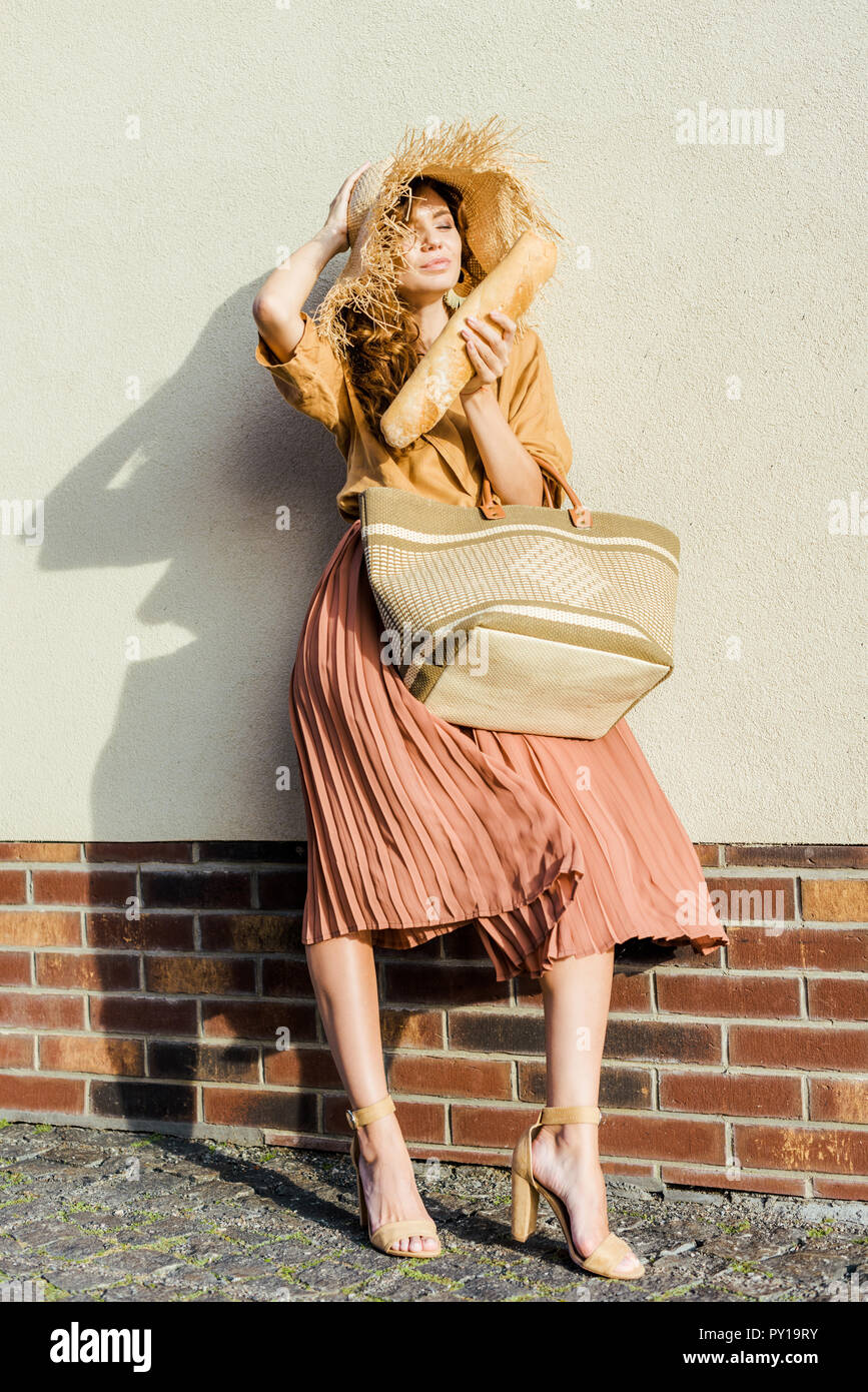 Schöne junge Frau im Stroh Hut mit Baguette stand vor der weißen Wand Stockfoto