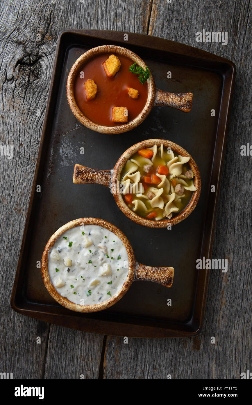 Ansicht von oben von drei Schüsseln Suppe auf ein Backblech. Verschiedene Suppen, Clam Chowder, Tomate und Chicken Noodle. Stockfoto