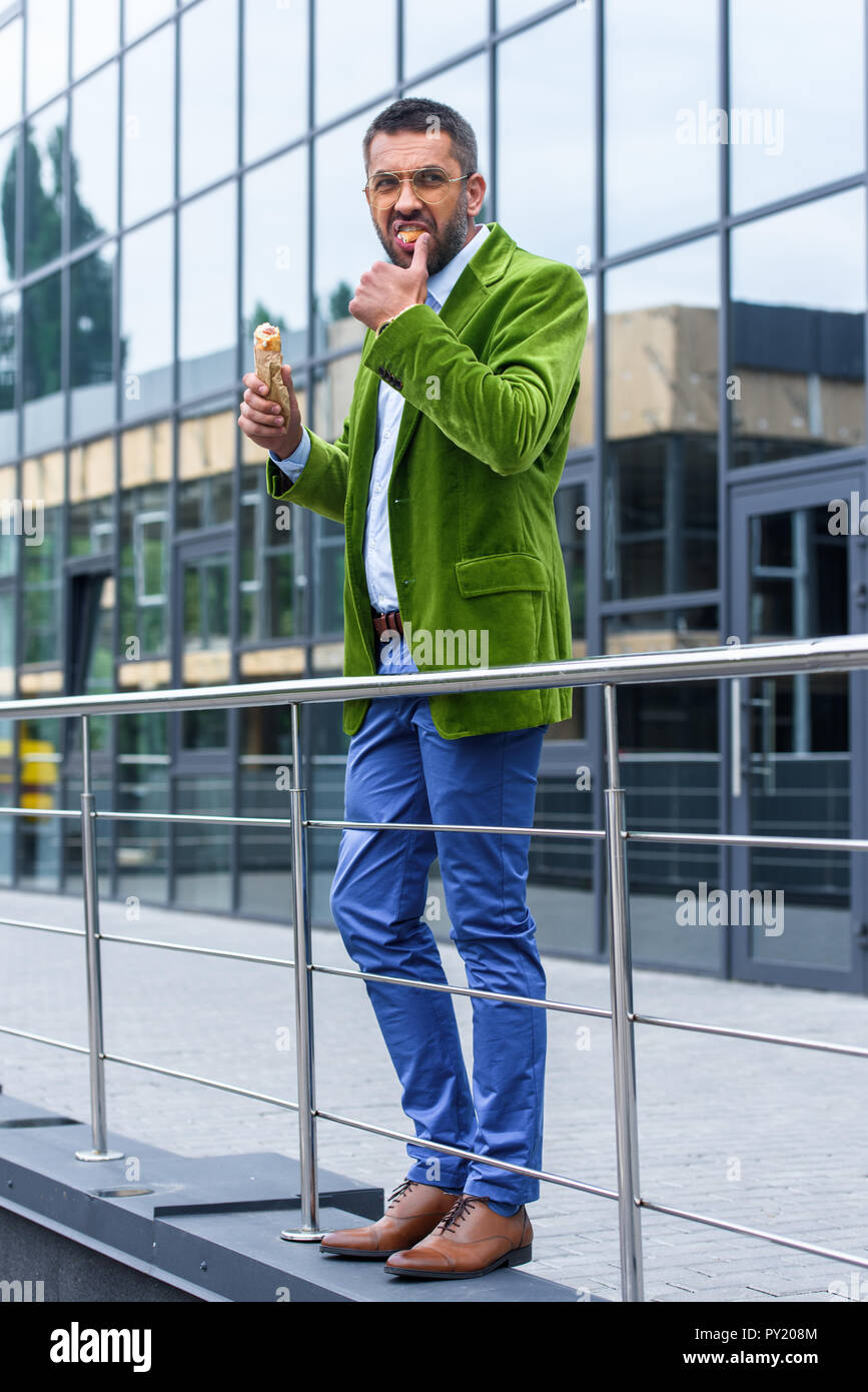 Seitenansicht des Menschen in grünem Samt Jacke essen französisch Hot Dog auf der Straße Stockfoto