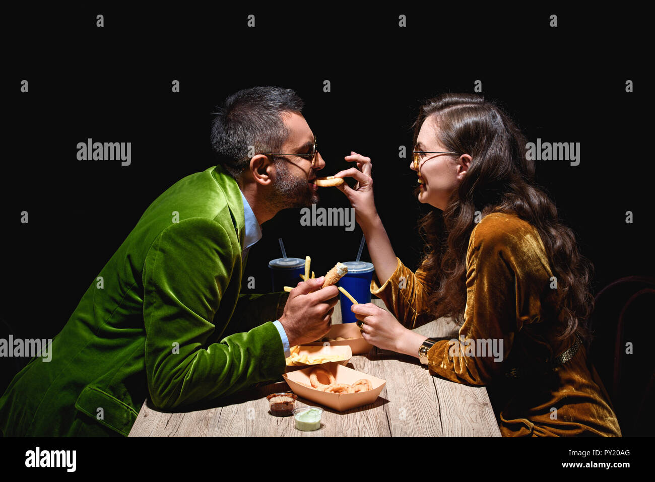 Seitenansicht des Paares in der stilvollen samt essen gebratene Zwiebeln, Pommes frites und Saucen am Tisch mit schwarzem Hintergrund Stockfoto