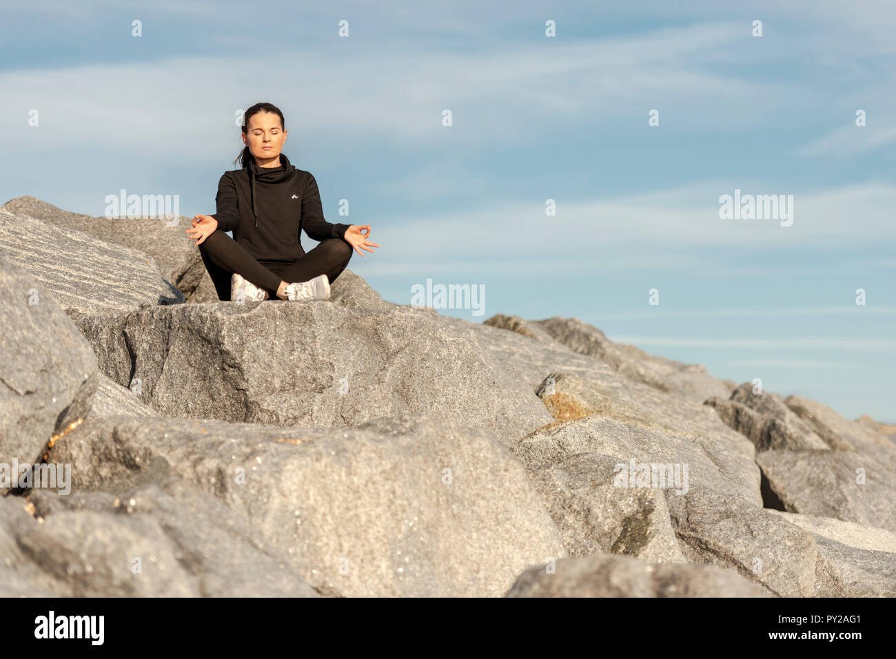 Frau sitzt auf Felsen mit Yoga und Meditation Stockfoto