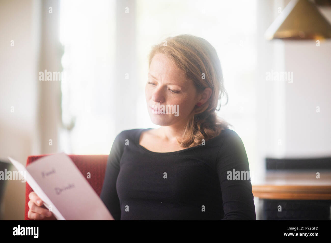 Frau sitzt in einem Hotelzimmer am Essen und Trinken Menü suchen Stockfoto