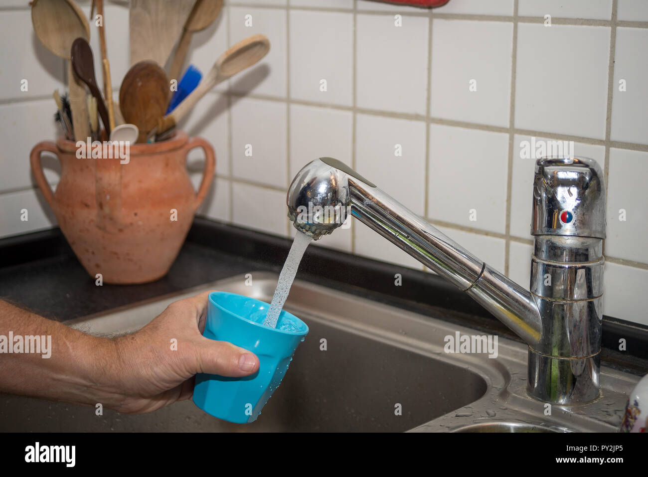 Des Menschen Hand Becher mit Wasser in einer Küche Stockfoto