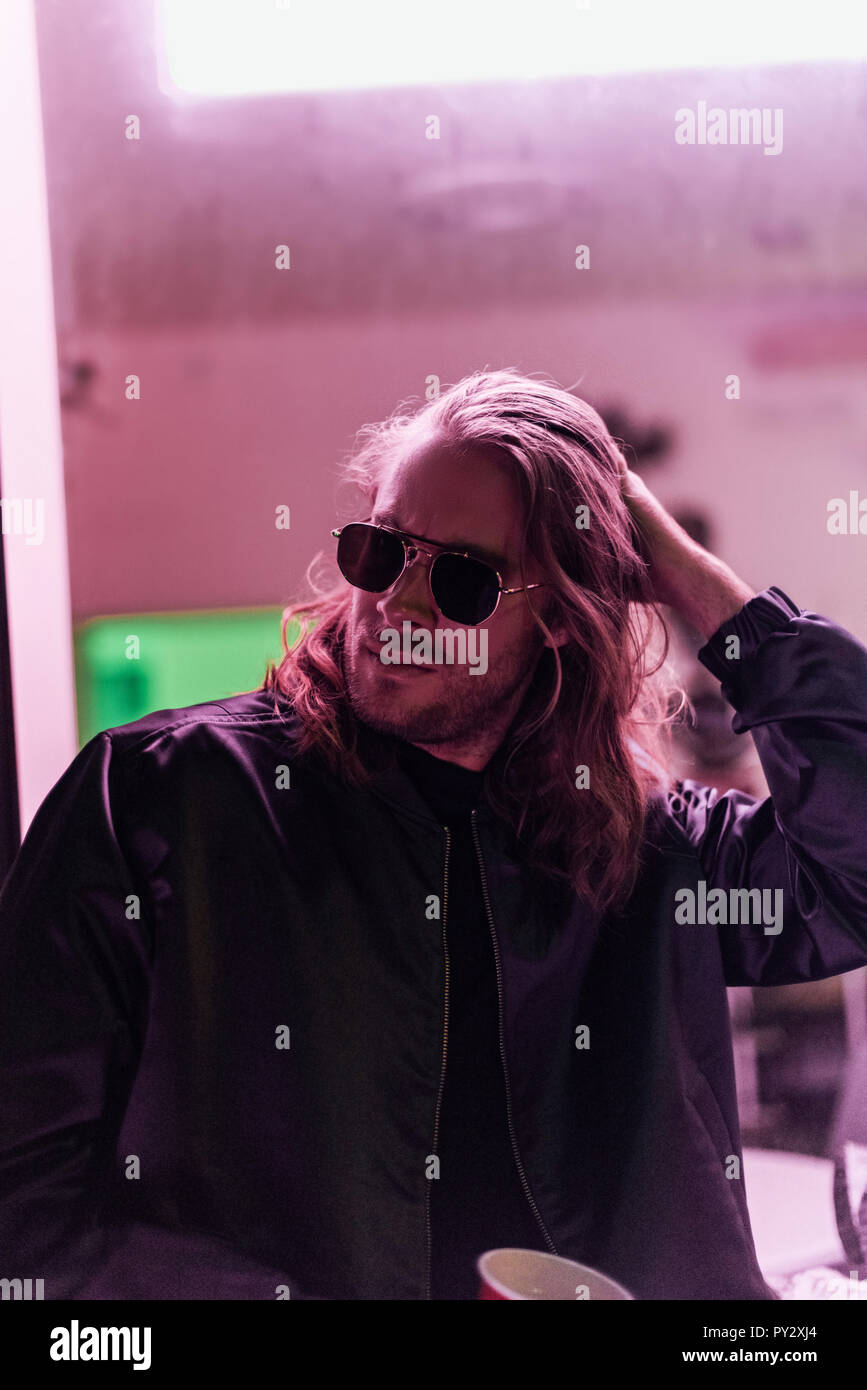 Hübscher junger Mann in der Lederjacke und Sonnenbrille Ausgabe Zeit auf der Straße in der Nacht unter rosa Licht Stockfoto